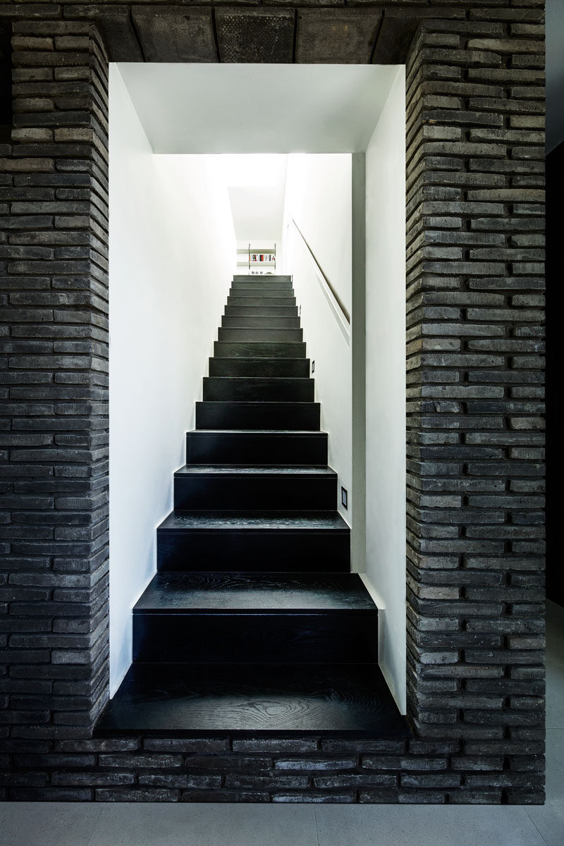 The stairs that lead up to the upper sections of this modern house have a monochrome appearance, with black stairs surrounded by white walls.