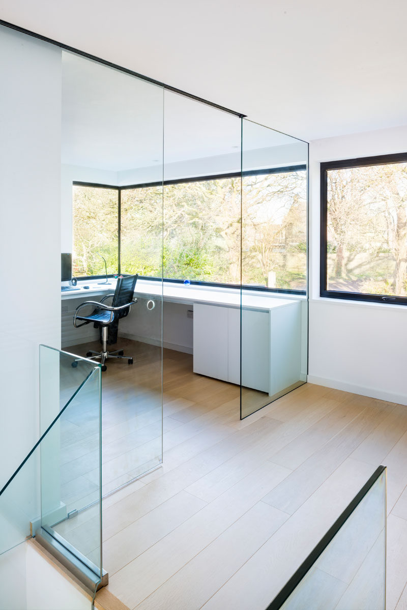 At the top of the stairs in this modern house is a home office with a glass wall and windows that look out to the surrounding landscape.