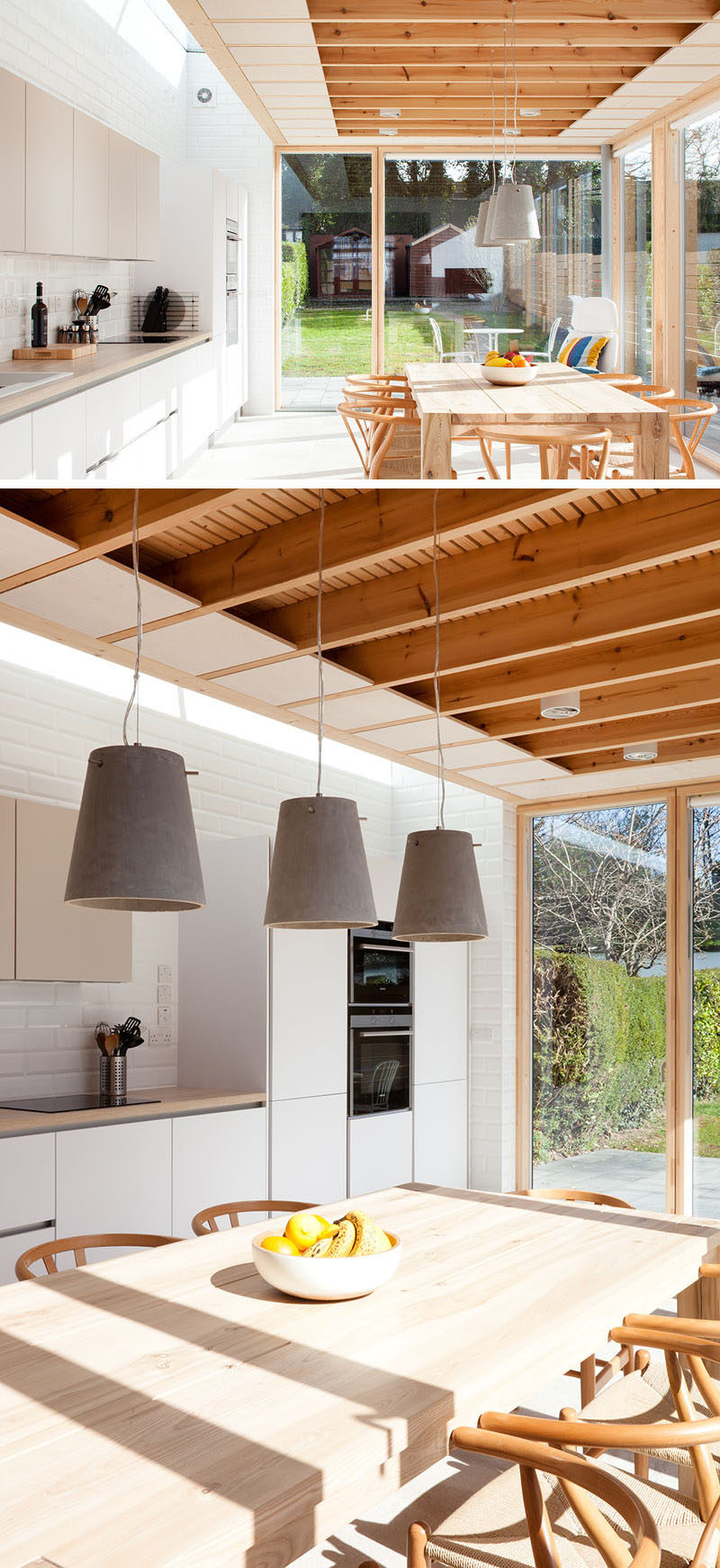 This modern house extension includes a dining table and a kitchen. Three concrete pendant lights anchor the dining table and chairs in the room.