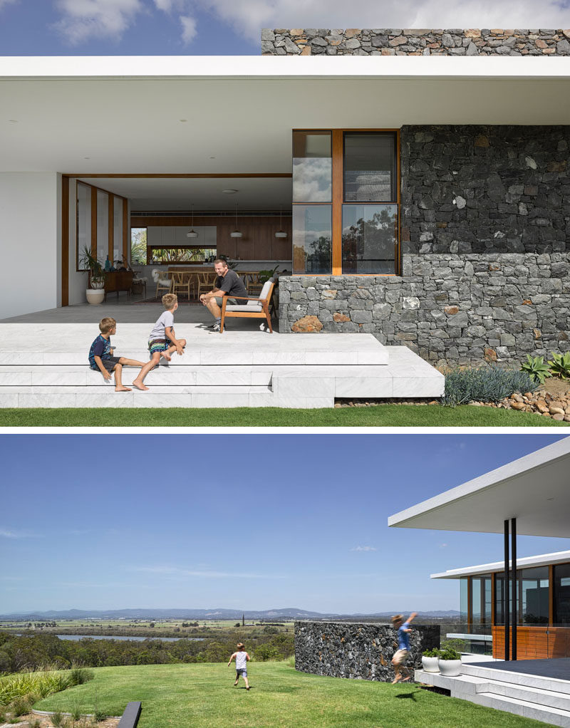 This modern house features a covered outdoor area with steps that lead down to the grassy backyard.