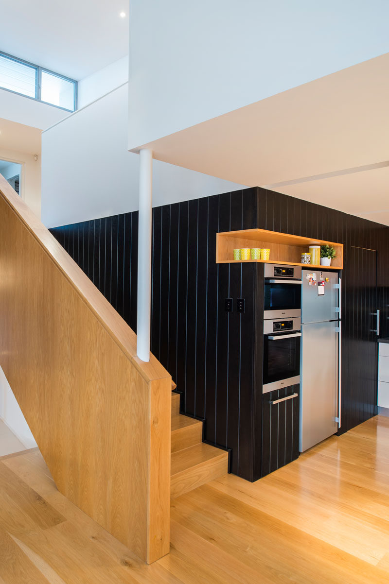 In this modern kitchen, a black accent wall is broken up by the use of a single wood shelf that's built into the wall and sits above the fridge.