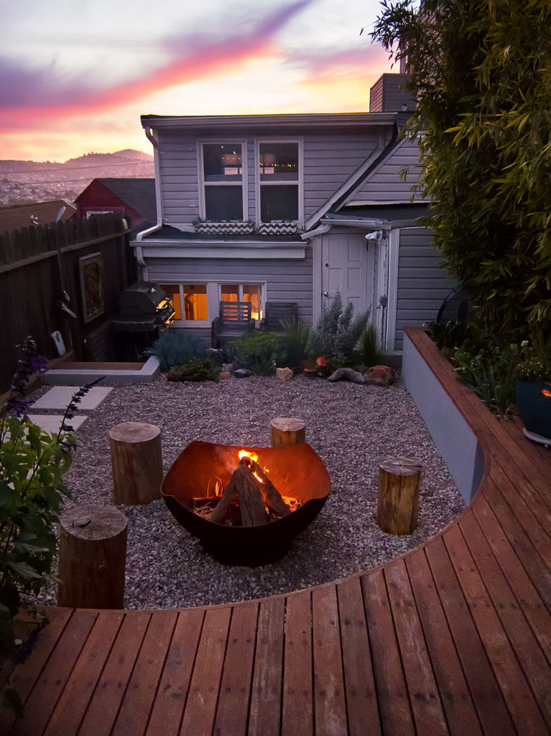 This modern landscaped backyard has a raised outdoor lounge deck, a wood burning firepit, succulents, bamboo and a vegetable garden.