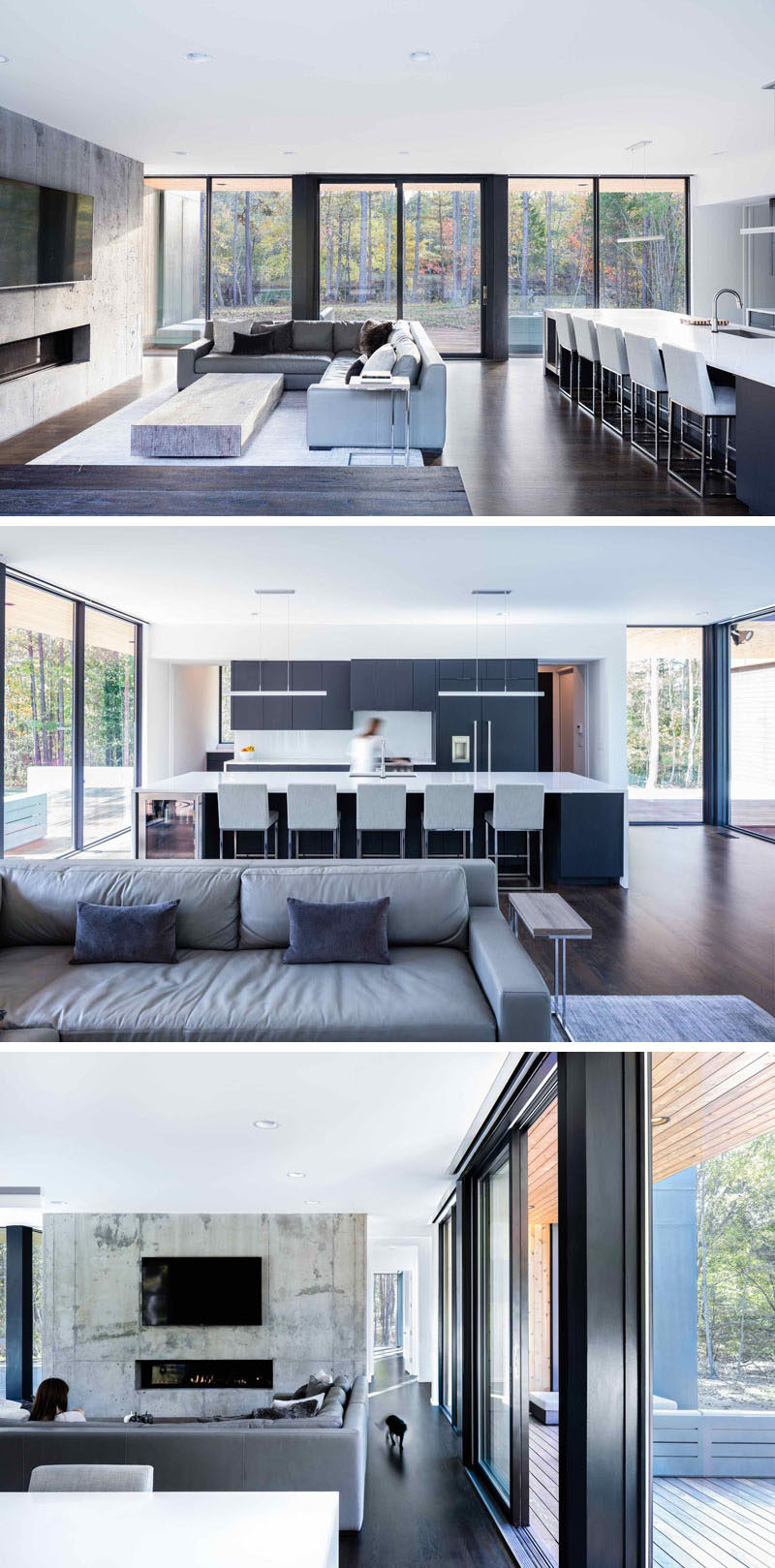 Inside this modern house, the living room and kitchen share the same space. The living room has the tv mounted on an exposed concrete wall that also features a fireplace, while the kitchen has a large island with seating, dark grey cabinets and white countertops.