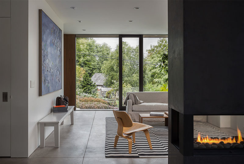 This modern house interior features a double-sided fireplace that can be enjoyed from both the dining room and the living room, while a large window provides views of the street and a nearby park.