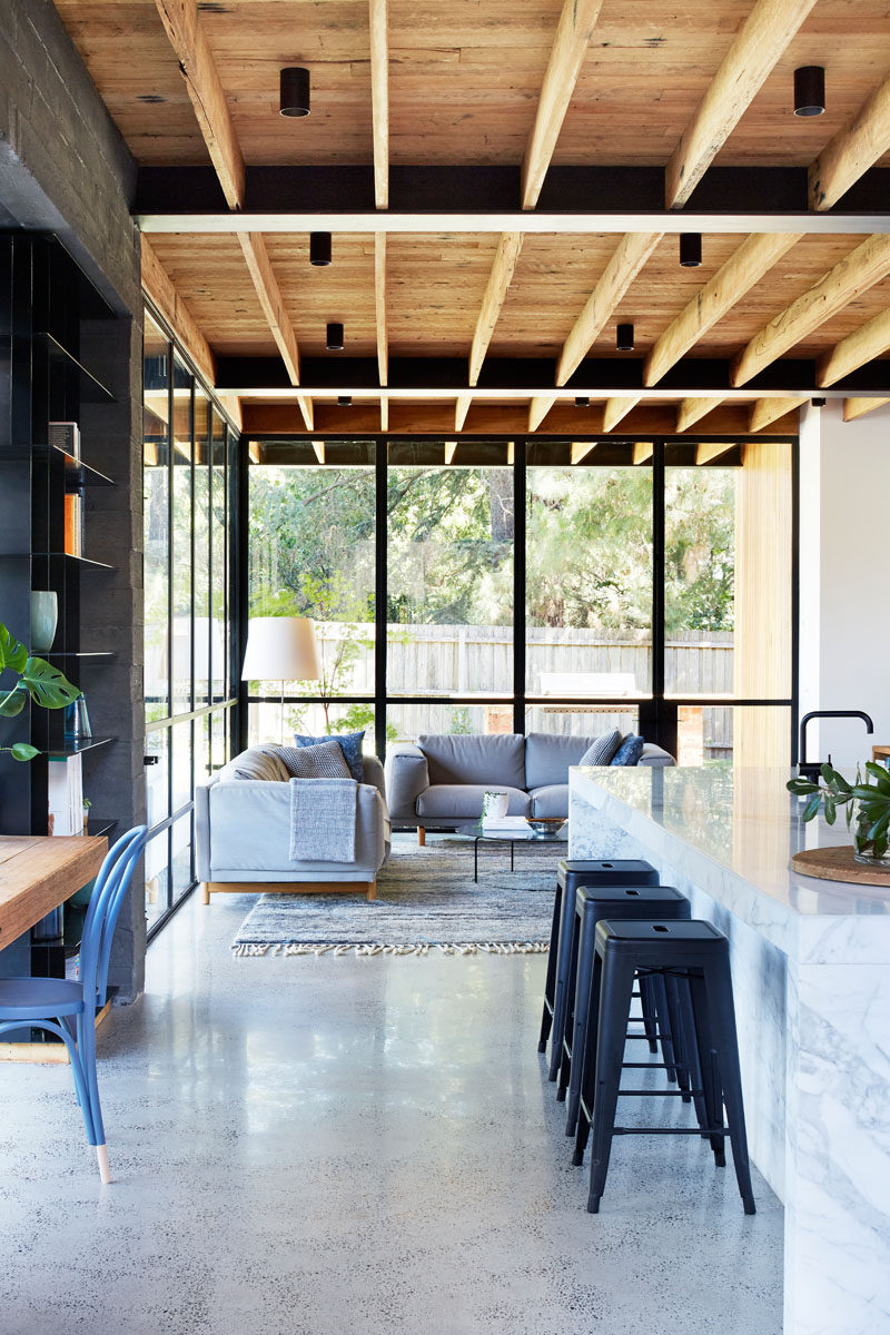 The interior of this modern house extension features materials that will age and patina over time, creating a sense of warmth. An exposed recycled wood ceiling runs the length of the living room and kitchen. 