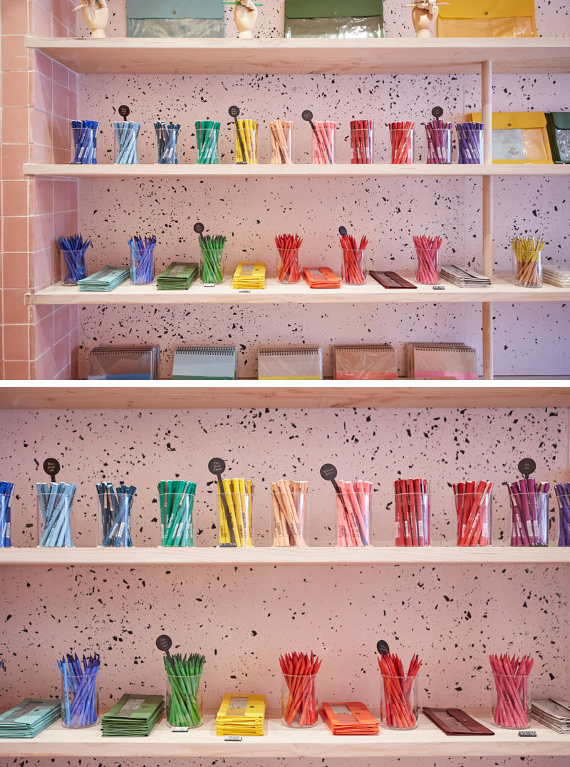 In this modern retail store, wood shelving has been used and embedded slightly into the tiled wall, while dowels support the shelves, and on the wall the jesmonite, with its freckled black and pink pigment, creates a unique backdrop for the colorful pens.