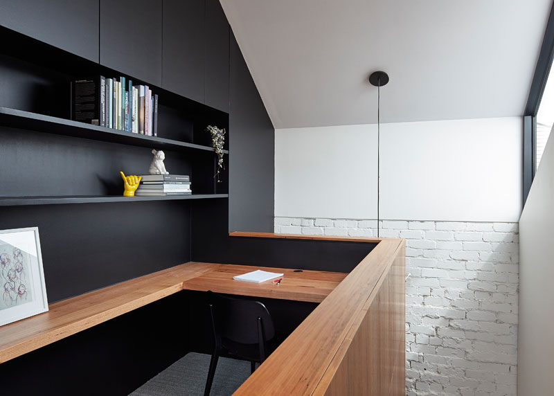 This modern home office features a built-in wood desk and black open shelving.