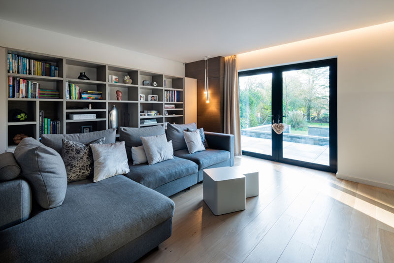 This modern house has a tv room with a large sofa and plenty of shelves for storing books and games.