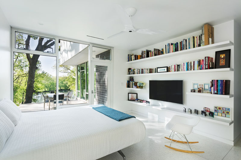 This modern master bedroom is located on the main floor of the home, with a wall of floating shelves surrounding a television. There's also access to the patio that sits off to the side of the living room.