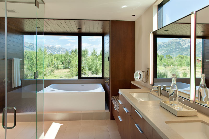 In this modern bathroom, multiple windows allow for plenty of natural light to fill the room, while the bathtub is surrounded by wood that wraps around from one wall to the other.