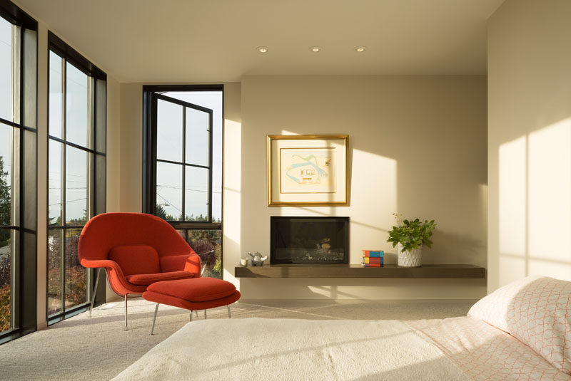 In this contemporary master bedroom, large grid windows provide plenty of natural light and fireplace make the room feel cozy, while the rest of the room has been kept neutral except for a bright Womb chair and ottoman.