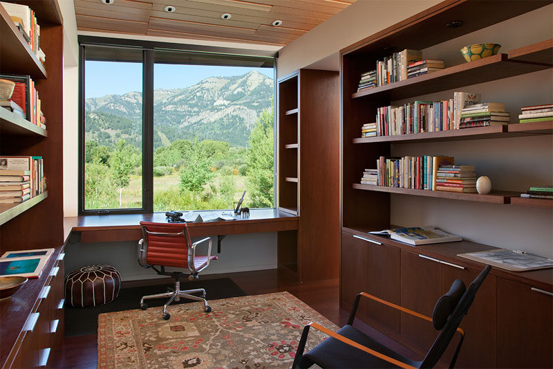 This modern home office features custom wood shelving that lines the walls and a desk has been positioned in front of the window to take advantage of the views.