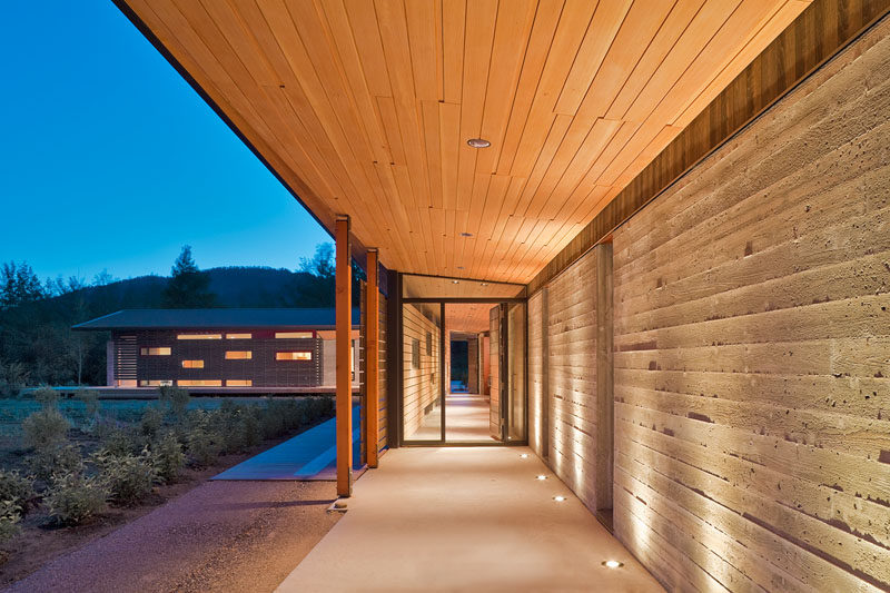 A board formed concrete wall highlighted by lighting and a wood overhang guide you to the front door of this modern mountain house.