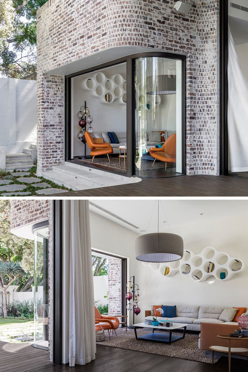 This modern house features a curved window and a sliding glass door surrounded by recycled brick, opens up the living room to the backyard. 