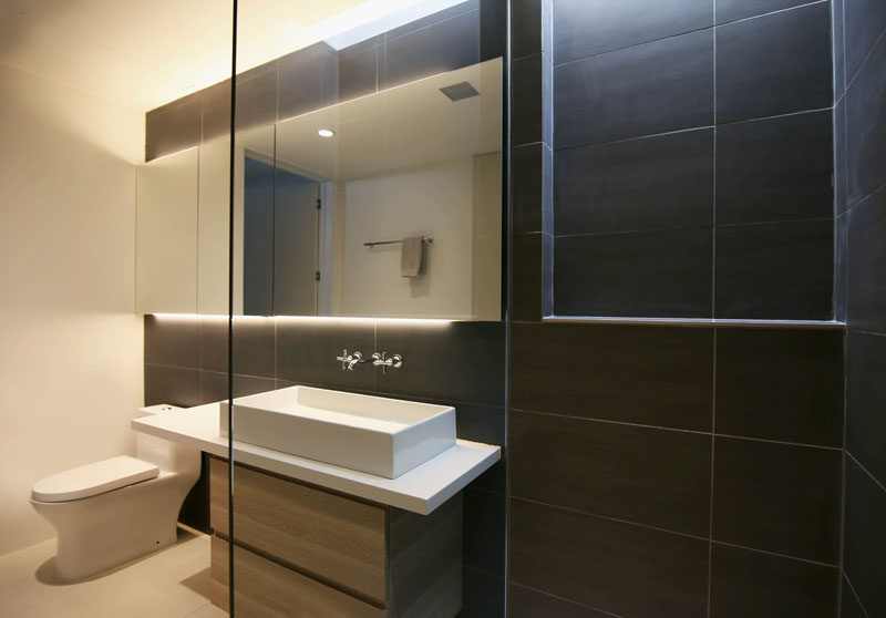 This modern bathroom uses dark tiles as an accent wall, while backlit mirror provides ambient light in the room. #ModernBathroom #tiles #bathroom