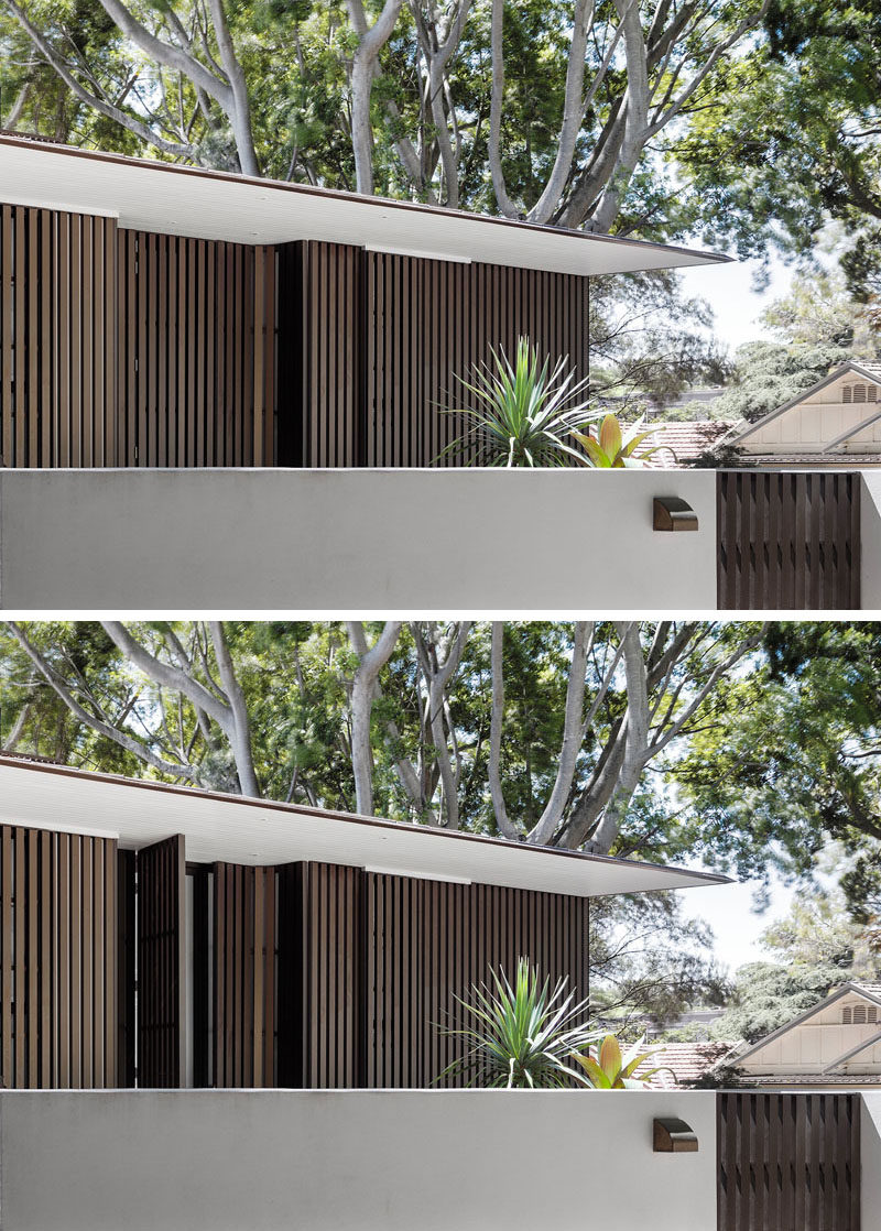 This modern house has a zinc roof that conceals gutters and down-pipes, creating a crisp exterior profile. The front door is hidden away from view within the anodized aluminum battens.