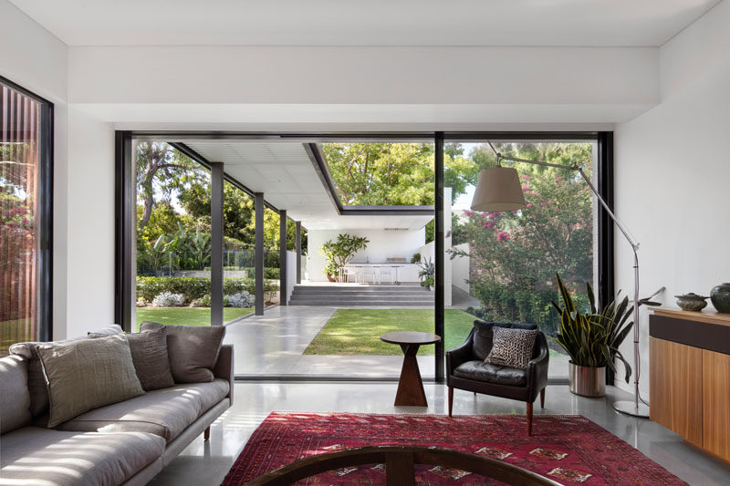 Concrete floors have been paired with white walls and black window / door frames to create a clean and modern aesthetic. The new living room opens up to the landscaped backyard through a large sliding glass door.