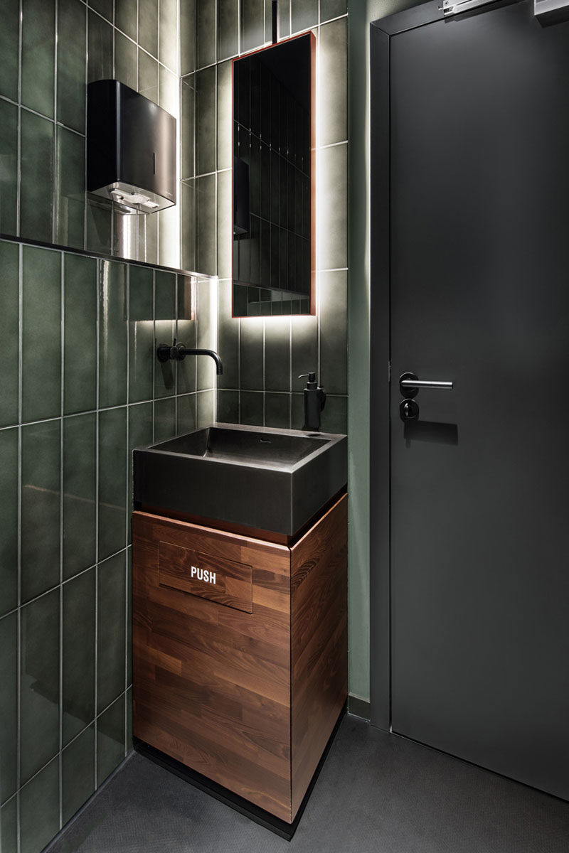 In this small bathroom, green tiles, wood and a backlit mirror reflect the design choices in this modern bar.