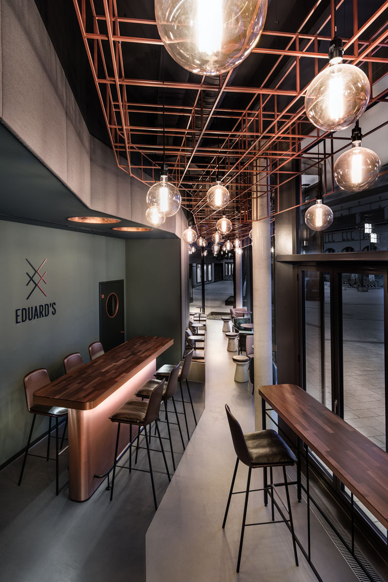 This modern bar has window seats that allow people to have a drink and watch the activities outside. The ceiling installation in the 16 foot (5m) high space consists of angular copper rods and eye-catching bulbs.