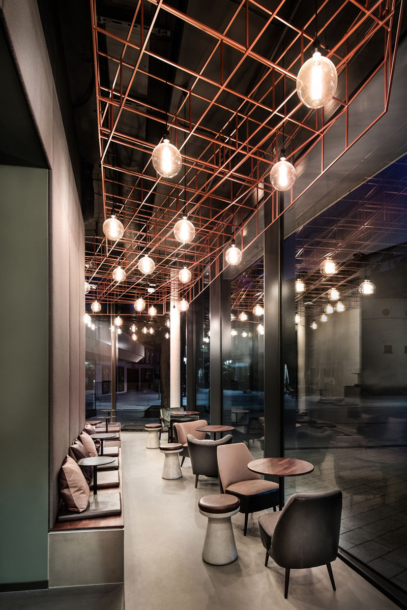 In this modern bar, one wall has a line of benches that use it as a backrest, while closer to the window, there's armchairs, both of which look out onto the outdoor patio. 