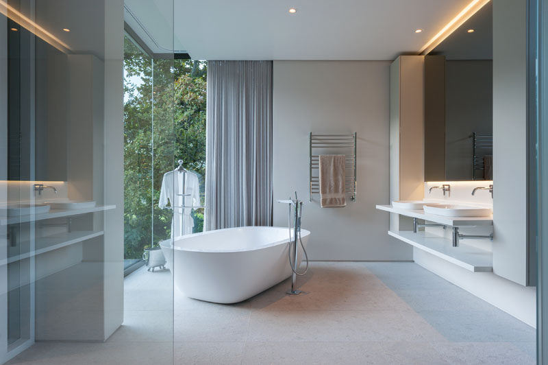 In this modern bathroom, a mirror with hidden lighting creates a calming atmosphere and the freestanding bathtub sits in front of the floor-to-ceiling windows to take advantage of the view.