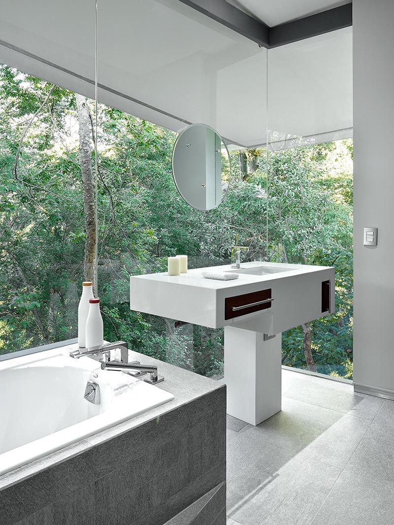 This modern bathroom features floor-to-ceiling glass walls that provide a view of the forest outside.