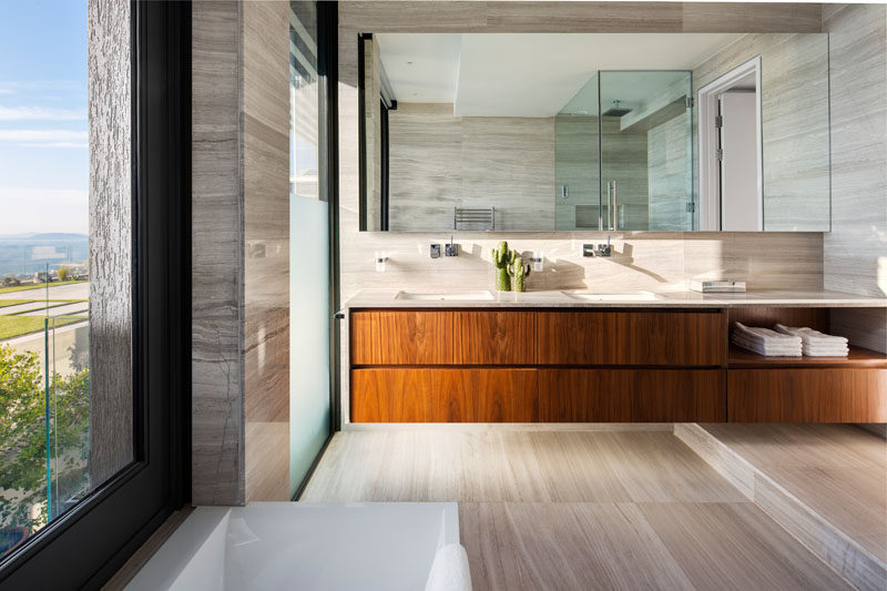 In this modern master bathroom, a long wood floating vanity with dual sinks provides storage, while windows provide water views.