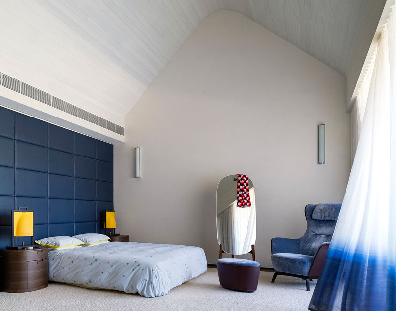 In this contemporary master bedroom, the double height ceiling features whitewashed timber boards, giving it a lofty appearance. 