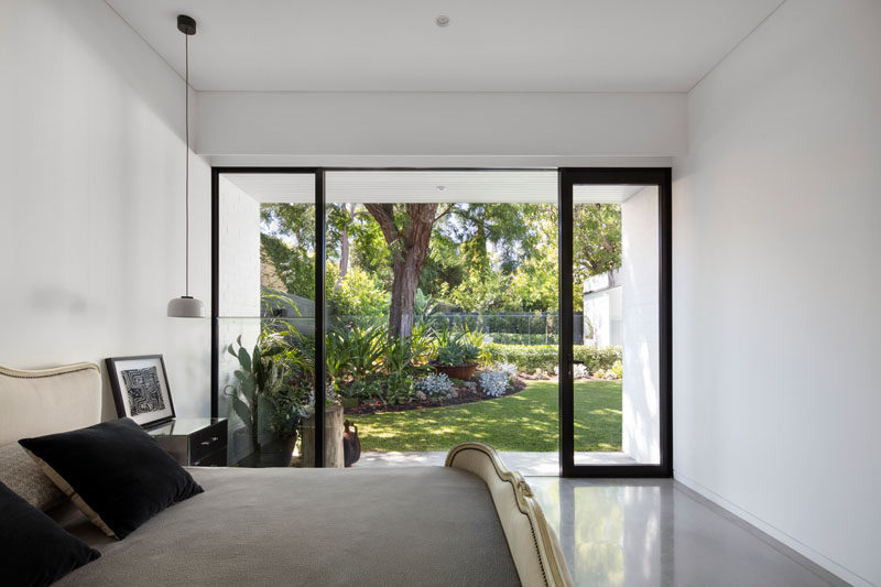 This simple white bedroom with concrete floors, opens up to a modern landscaped backyard with swimming pool.