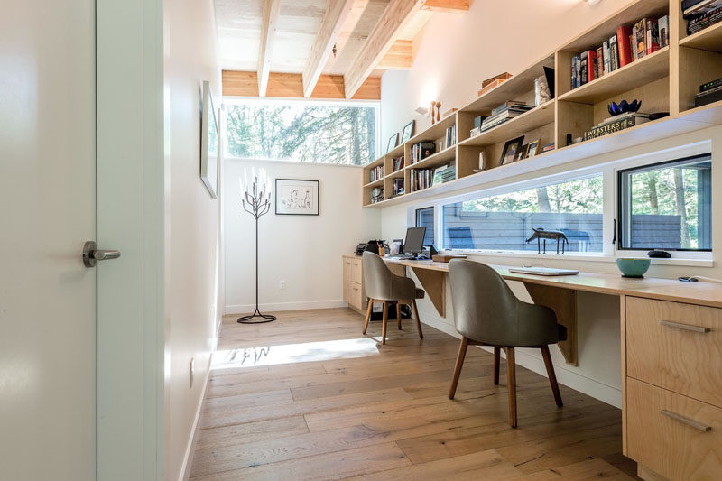 In a hallway next to one of the bedrooms in this modern house, there's a small home office area. Built-in furniture and shelving makes the space suitable for two people and a window provides views outside.