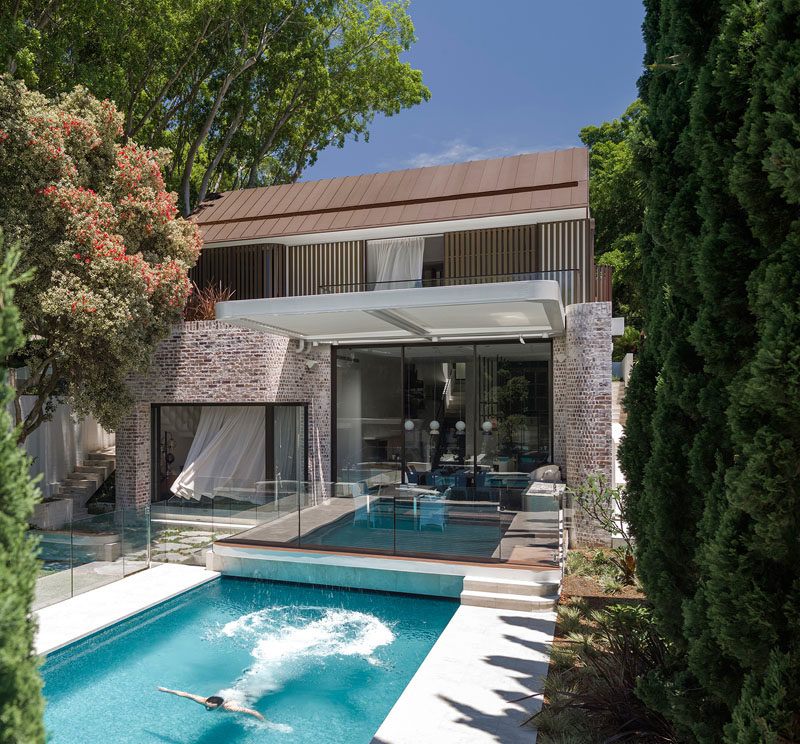 At the rear of this modern house, Pencil Pines flank the swimming pool and deck in the backyard. Above the deck there are rotating blades on the motorized pergola, allowing the home owner to control the amount of shade needed.