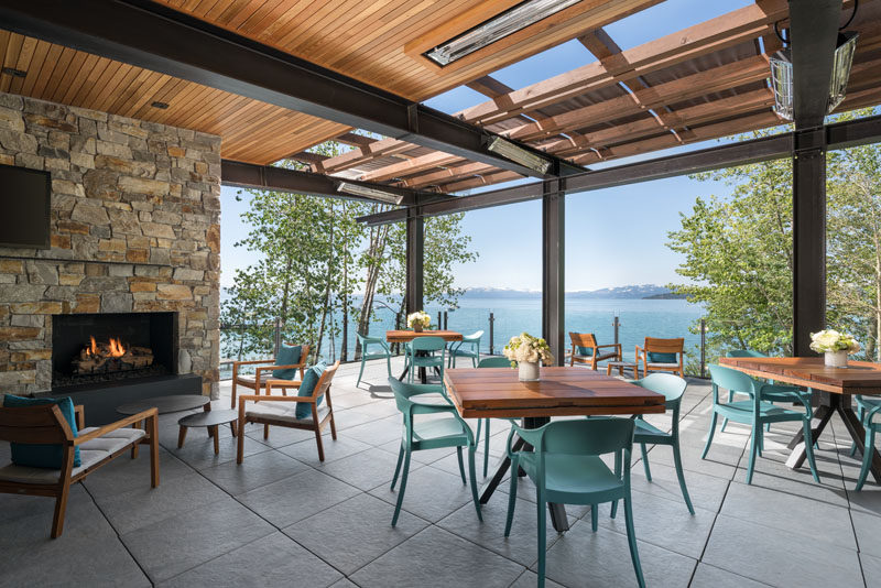 The upper floor of this modern lakeside club house features a fireplace with a stone surround, and a covered dining deck with expansive views of the lake.