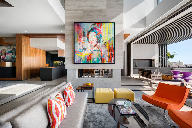 In this modern living room, there's a double-sided fireplace with a bright colorful piece of artwork to draw your attention. This also compliments the other brightly colored furnishings in the space.