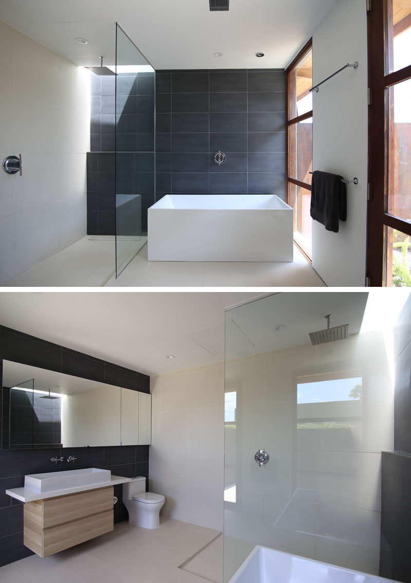 In this master bathroom, dark tiles have been used to create an accent wall, while a glass partition separates the shower from the bathtub. The dark tiles have also been used on the wall behind the mirror and vanity. #MasterBathroom #EnsuiteBathroom #DarkTiles #ModernBathroom #bathroom