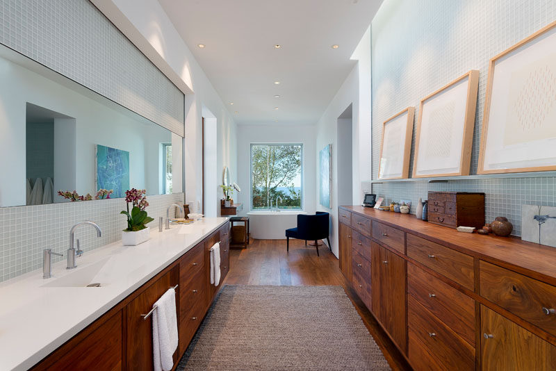 In this modern master bathroom, there's wood cabinetry for plenty of storage, a double-sink vanity and the bath is positioned beneath a window at the end of the room.