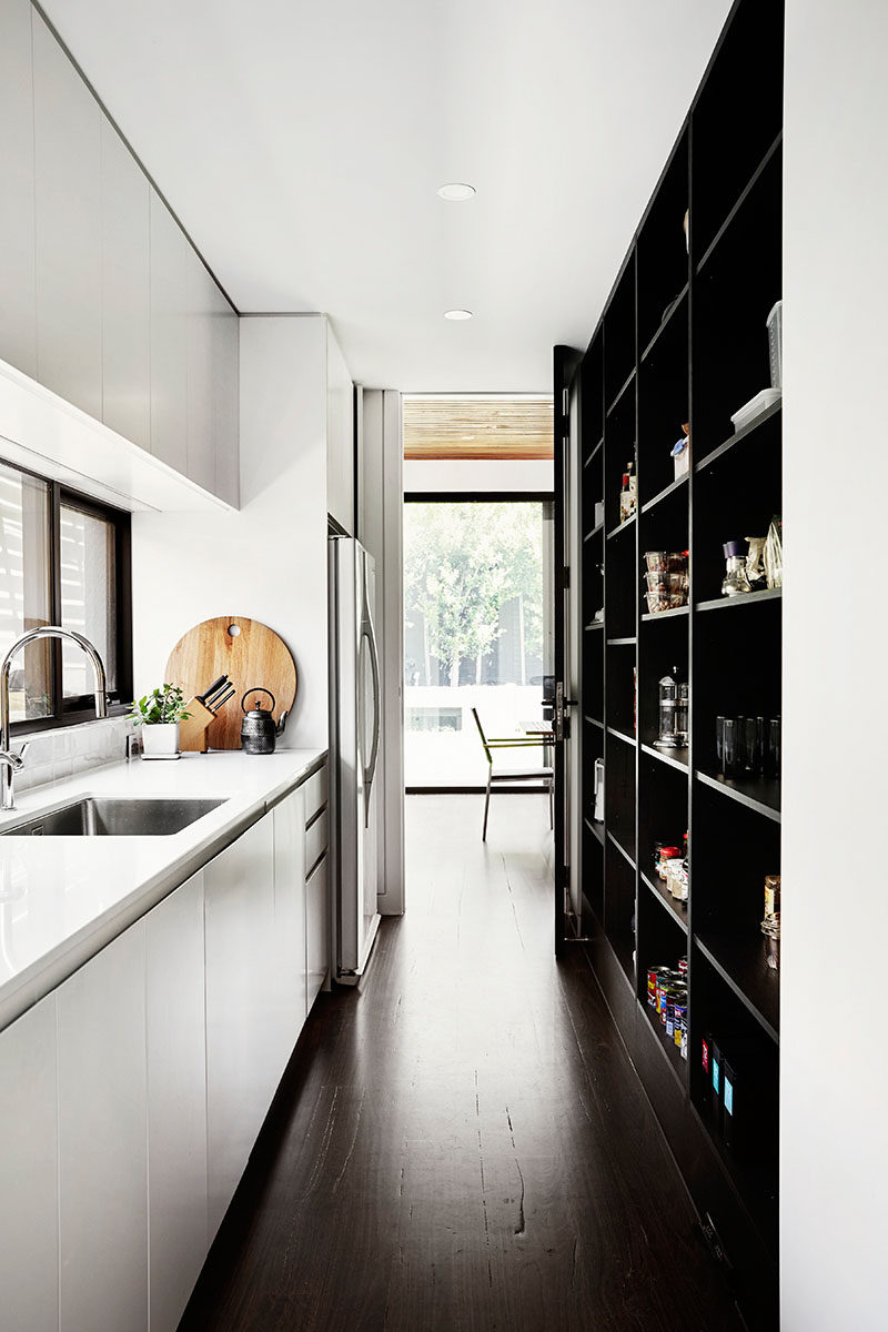 This modern pantry hides the fridge from the main living area. Dark built-in open shelving and additional cabinets provide ample storage.