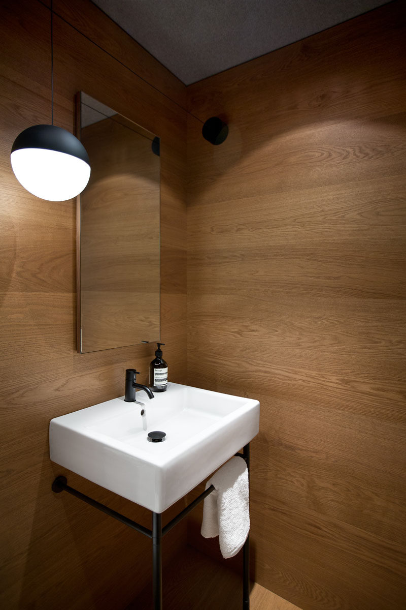 In this modern powder room the walls are lined in wood. A simple sink with a black frame matches the pendant light hanging beside the mirror.