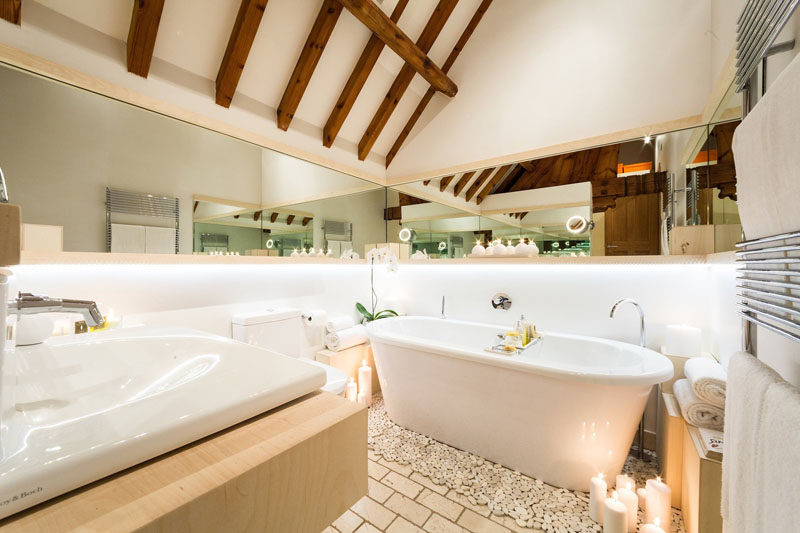 In this modern bathroom, a freestanding tub sits below a lofted ceiling, and a mirror that wraps around the wall makes the room feel larger. #ModernBathroom #Bathroom #Mirrors #FreestandingBathtub