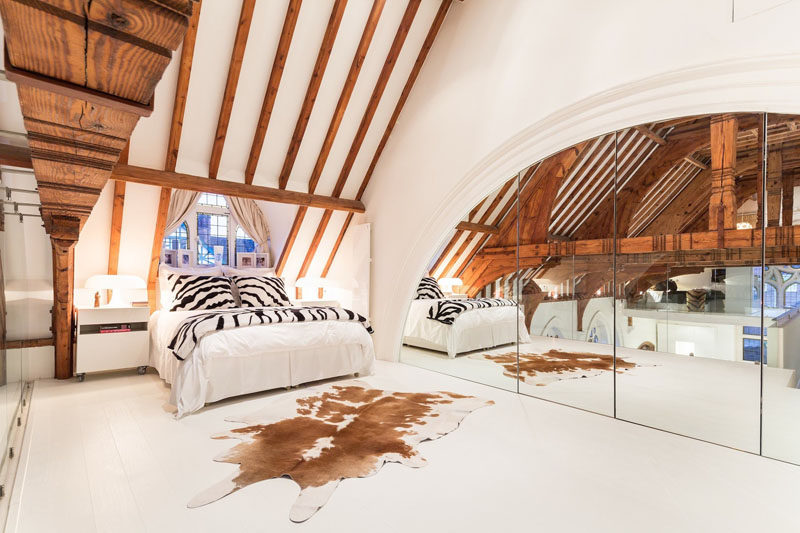 This modern bedroom in a renovated church features a wall of mirrors to reflect the interior. #RenovatedChurch #ChurchConversion #WoodBeams #ModernBedroom #InteriorDesign #Mirrors