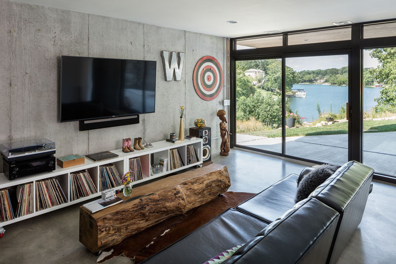 This modern lakeside house has tv room with a raw concrete wall on the lowest level of the house, and it also has direct access to the backyard.