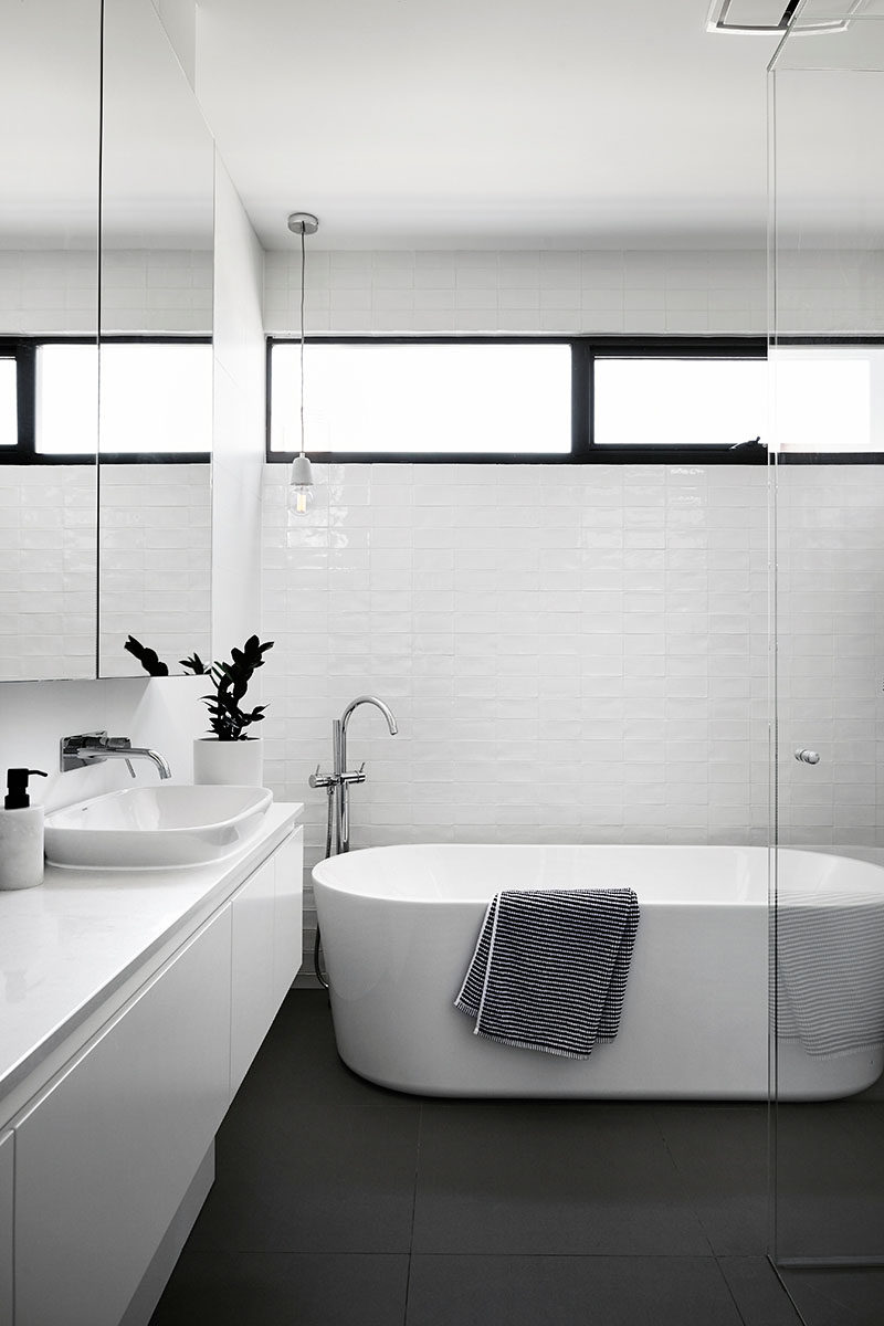 This modern and simple black and white bathroom has slightly textured white tiles, a standalone bathtub and a walk-in glass shower.