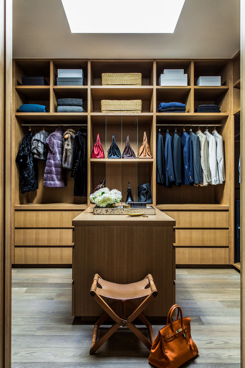 This modern walk-in closet with a skylight is filled with plenty of open shelving, cabinets and an accessory island. #WalkInCloset #ClosetIdeas