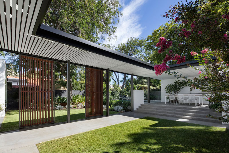 This modern backyard has a covered walkway that connects the house to a raised outdoor kitchen / dining area and pool..