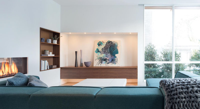 In this modern living room, a wood-lined bookcase has been built into the wall next to the fireplace. #LivingRoom #BuiltInBookshelf #WoodLinedShelves #InteriorDesign