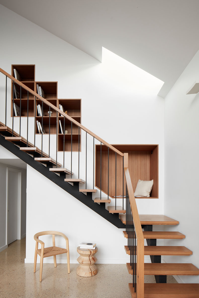 Wood-lined bookshelves and a seating nook have been built into the wall next to this modern staircase. #shelving #BuiltInShelving #WoodLinedShelving