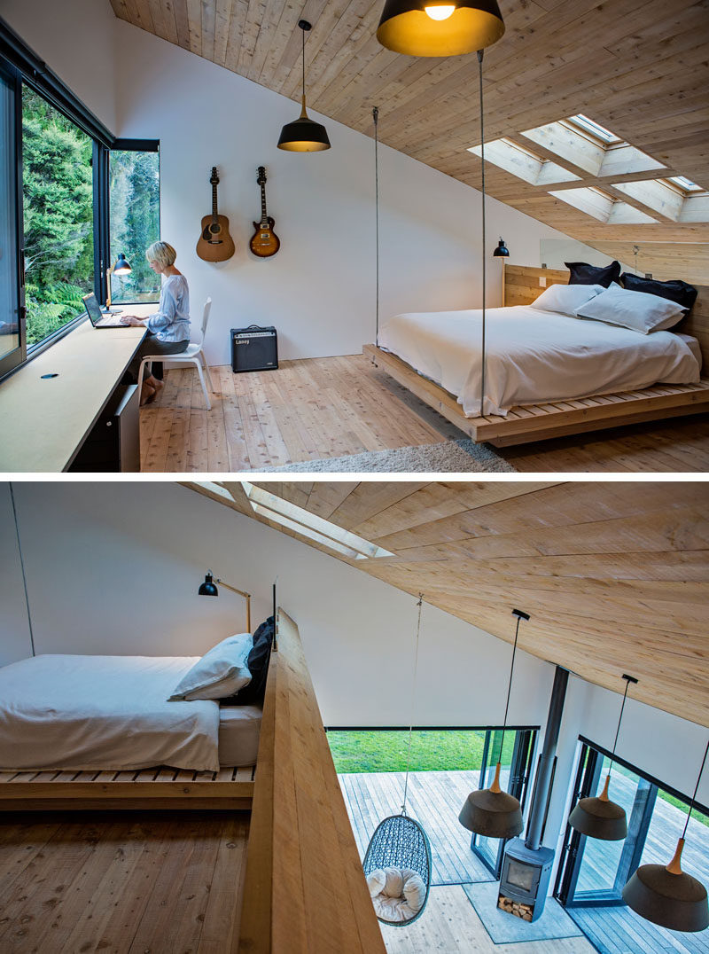 The mezzanine in this modern house is home to a bedroom. Four skylights are positioned above the bed, which is partially suspended from the sloped ceiling. From behind the bed you can see the living room below. #Mezzanine #ModernBedroom #Skylights #ModernInteriorDesign