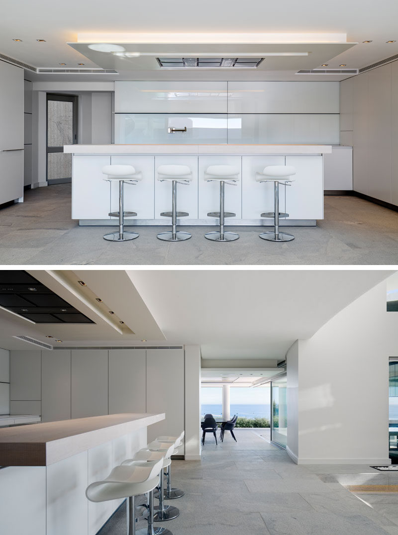 This modern house has a minimalist kitchen that has a light, neutral palette with white walls and cabinets, and grey floors. #MinimalistKitchen #WhiteKitchen #KitchenDesign