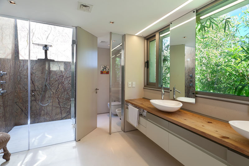 In this modern master bathroom, a large wood vanity looks out to the garden, while the glass enclosed shower has a skylight. #MasterBathroom #DoubleVanity #GlassEnclosedShower #InteriorDesign