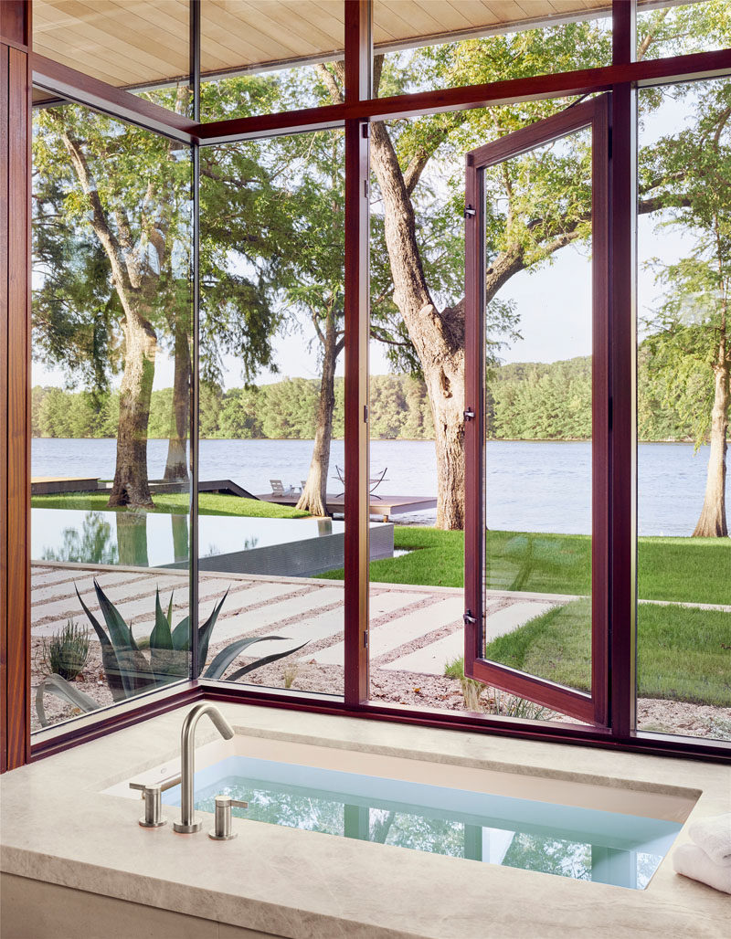 In this modern master bathroom, a deep soaking tub has plenty of windows that provide natural light and views of the lake. #Bathroom #SoakingTub #Windows #ModernBathroom