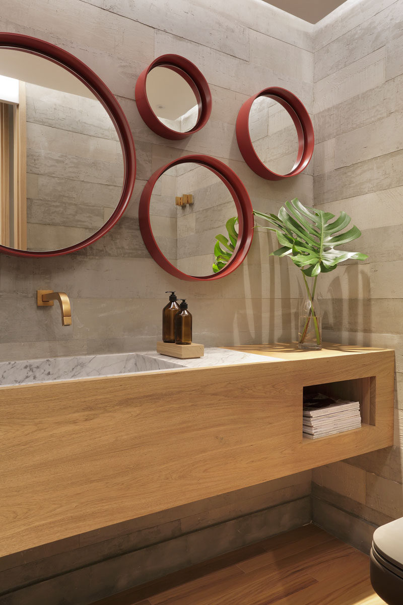 In this modern bathroom, multiple round mirrors with red frames act like an art installation, while a wood vanity and palm frond add a natural touch. #ModernBathroom #BathroomDesign #RoundMirrors
